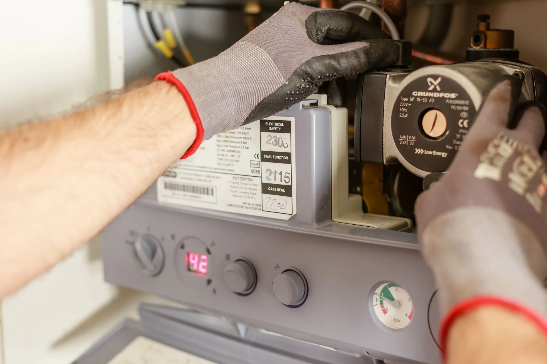 An engineer's gloved hands servicing the inside of a Potterton combi boiler