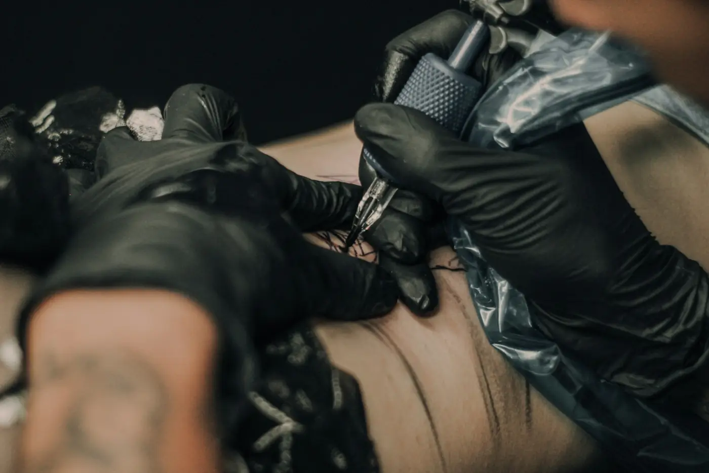 Tattoo artist in black gloves working on a client's arm