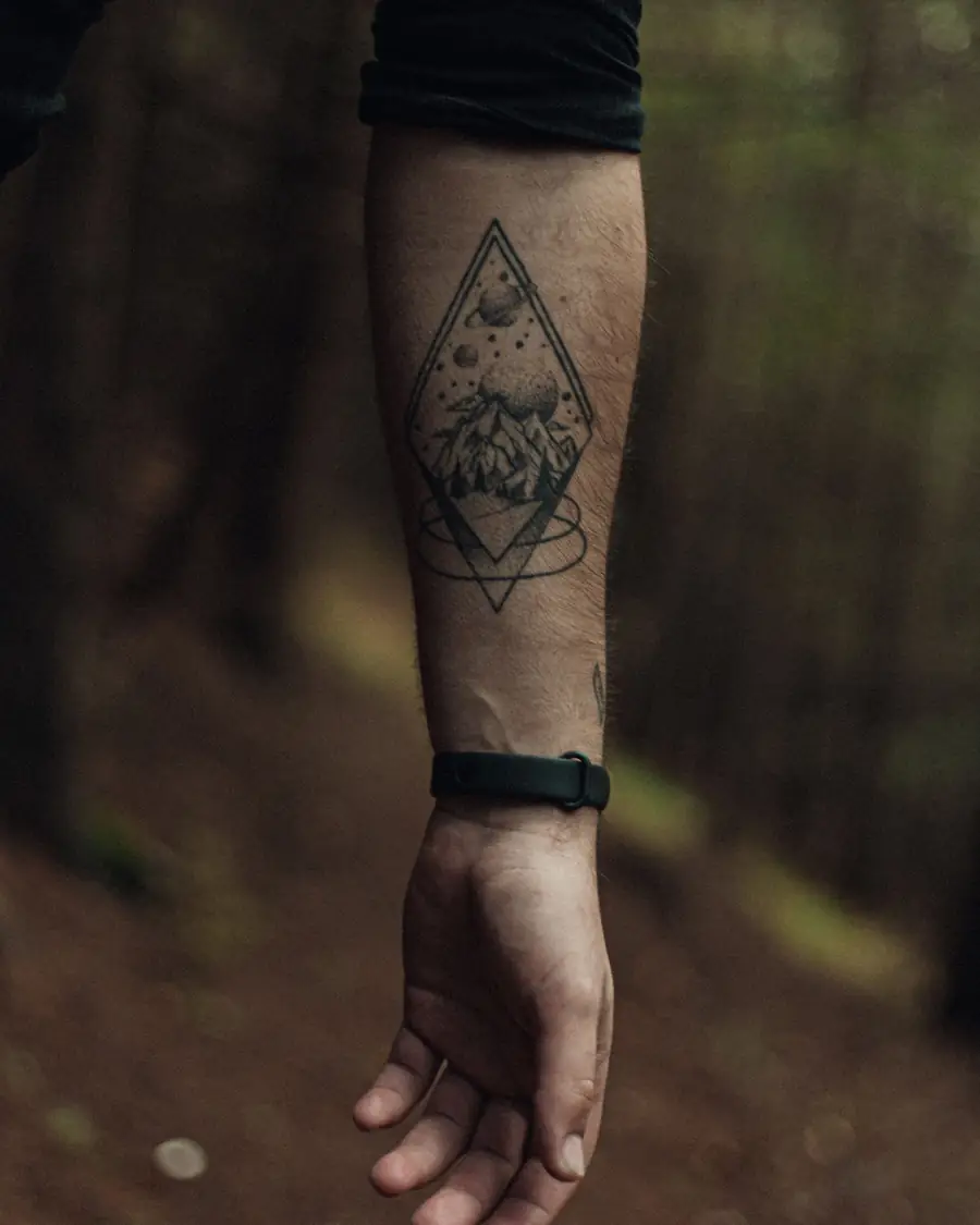 Geometric diamond framing a line-drawn landscape on the inner forearm