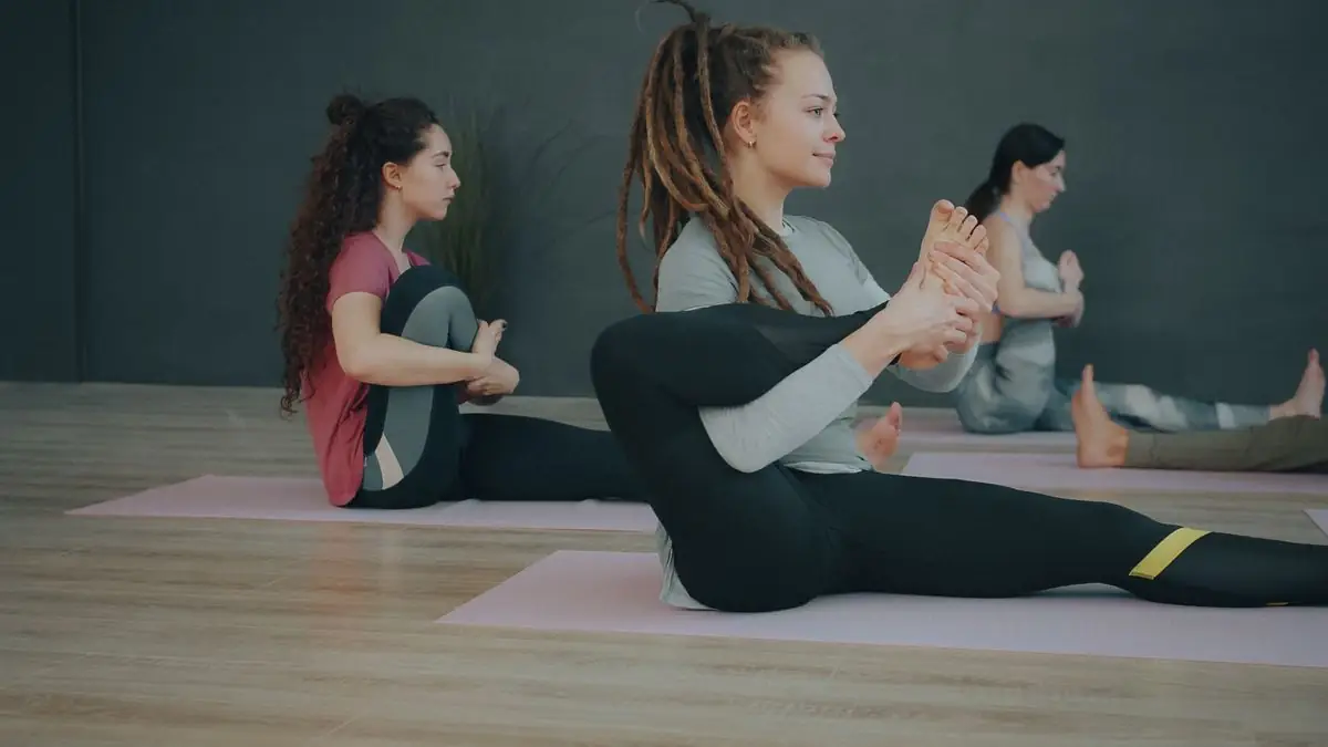 Three women doing a seated hip stretch against a dark wall